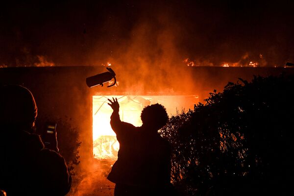 Протестующий бросает огнетушитель в горящее здание во время демонстрации в связи со смертью Джорджа Флойда, убитого полицейским (29 мая 2020). Миннеаполис - Sputnik Армения