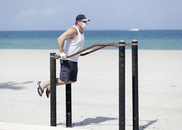 Мужчина в защитной маске во время выполнения упражнений на турнике на пляже в Голливуде, США - Sputnik Армения
