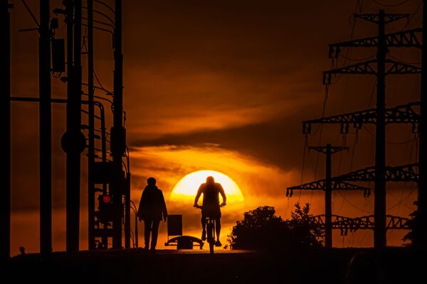 Мужчина едет на велосипеде по одной из улиц в Москве на фоне заката - Sputnik Армения