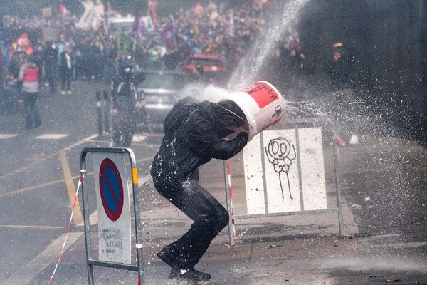 Протестующий прикрывается ведром от удара водяной пушкой, которую полицейские используют для разгона акции протеста медработников в Нанте - Sputnik Армения