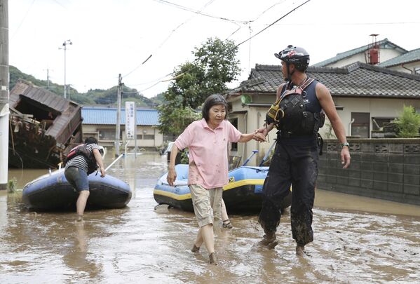 Спасатель помогает женщине во время эвакуации в японской префектуре Кумамото - Sputnik Армения
