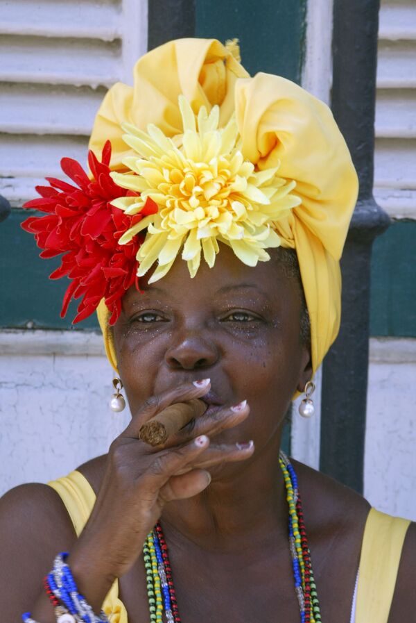Кубинка курит сигару на одной из улиц старой Гаваны. Женщины на Кубе всегда отличались оригинальной внешностью и свободой. На улицах столицы днем можно встретить кубинок с повязкой на голове. Дело в том, что под повязкой женщины часто скрывают накрученные на бигуди волосы, которые к вечеру, перед выходом в свет, превратятся в прическу. - Sputnik Армения