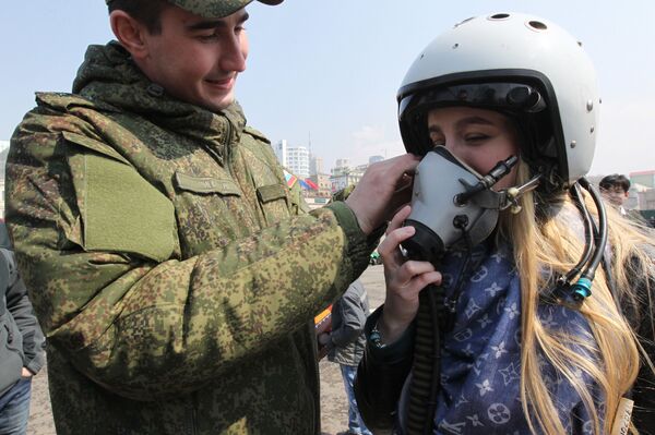 Военнослужащий помогает девушке примерить летный шлем на выставке боевой техники на центральной площади Владивостока - Sputnik Армения